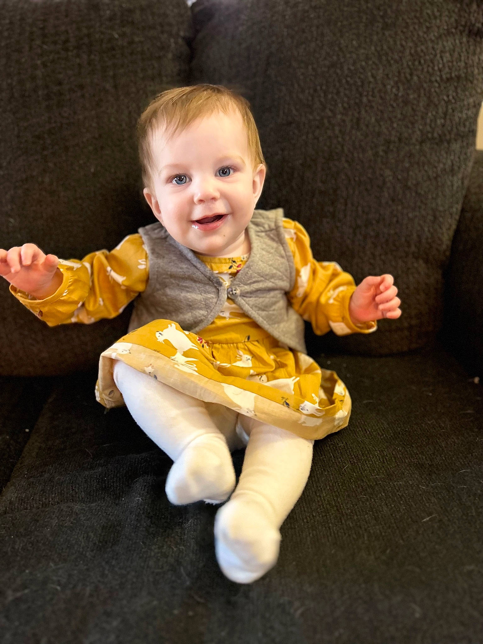 Freyja is registered to the contest to win money with this photo: baby, baby_toddler_clothing, cheek, comfort, couch, eye, finger, flooring, fun, gesture, hand, happy, human_body, joy, lap, person, sitting, sleeve, smile, textile