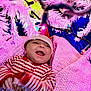 baby, smiling, christmas, holiday, festive, santa_hat, striped_clothing, blanket, pink_lighting, decorations, christmas_tree, lights, happy, infant, indoors, cute, holiday_season, celebration, child, portrait