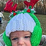 Spencer is registered to the contest to win money with this photo: baby, child, hat, knit_hat, earmuffs, reindeer_antlers, red, green, white, face, blue_eyes, outdoor, forest, winter, holiday, festive, person, blurred_background, closeup, cute