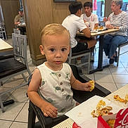 Rome is registered to the contest to win money with this photo: toddler, child, high_chair, fast_food, restaurant, food, eating, table, indoor, people, casual, plate, napkin, sauce, clothing, face, floor, chair, window, conversation
