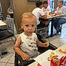 toddler, child, high_chair, fast_food, restaurant, food, eating, table, indoor, people, casual, plate, napkin, sauce, clothing, face, floor, chair, window, conversation