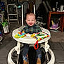 Walker is registered to the contest to win money with this photo: baby, walker, toy, smile, boots, indoor, child, plaid_shirt, carpet, furniture, table, chair, living_room, person, flooring, happy, clothing, face, footwear, infant