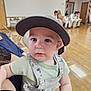 Walker joined the competition — help win amazing prizes! baby, child, cap, hat, overalls, dinosaur_pattern, indoor, person, holding, seated, group, floor, wooden_floor, blurred_background, people, casual_clothing, infant, cute, young_child, portrait