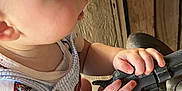 Walker is registered to the contest to win money with this photo: baby, child, hands, face, curious, superman, clothing, mechanical_object, rustic, texture, closeup, profile, indoor, person, young_child, grip, expression, exploration, cute, toddler