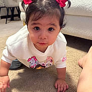 Luna is registered to the contest to win money with this photo: toddler, child, crawling, carpet, pigtails, red_bows, sweatshirt, cartoon_print, indoors, living_room, couch, pillow, curious, cute, person, young_child, face, hand, foot, home