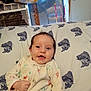 baby, bed, blanket, cheerful, child, cozy, cute, face, fish_pattern, happy, head, indoor, infant, lying_down, onesie, person, pillow, room, sleepwear, smiling