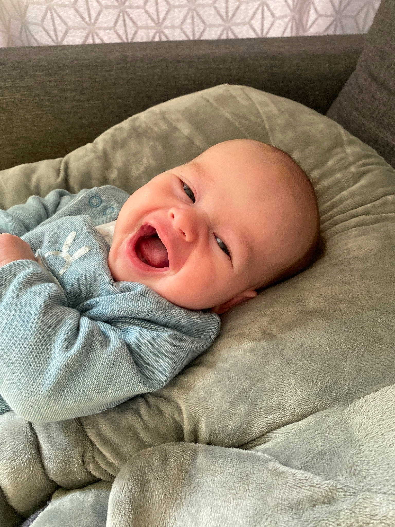 Tao participe au concours pour gagner de l'argent avec cette photo : baby, baby_toddler_clothing, bedding, bedtime, cheek, child, comfort, eye, grey, linens, pattern, person, portrait_photography, room, sitting, sleeve, smile, textile, toddler