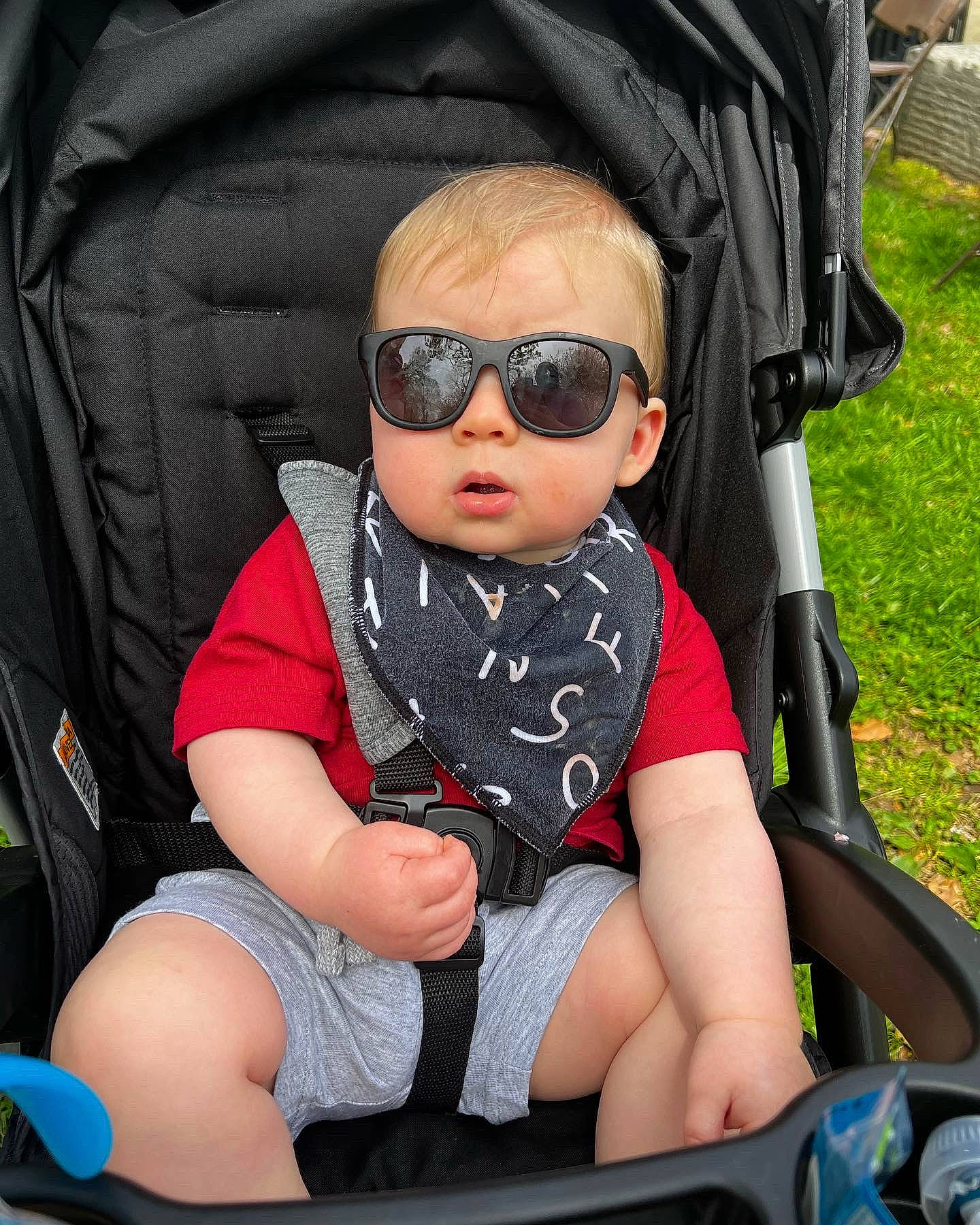 Archie is registered to the contest to win money with this photo: auto_part, baby, baby_carriage, baby_toddler_clothing, black, car_seat, comfort, eyewear, goggles, grass, mouth, person, personal_protective_equipment, photograph, seat_belt, sleeve, sunglasses, thigh, toddler, vision_care