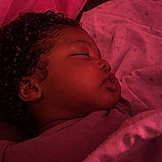 Russell is registered to the contest to win money with this photo: baby, bed, blanket, close_up, cozy, curled_hair, curly_hair, eyes_closed, face, indoors, infant, nap, peaceful, pink, portrait, profile, red_lighting, resting, sleeping, soft_texture