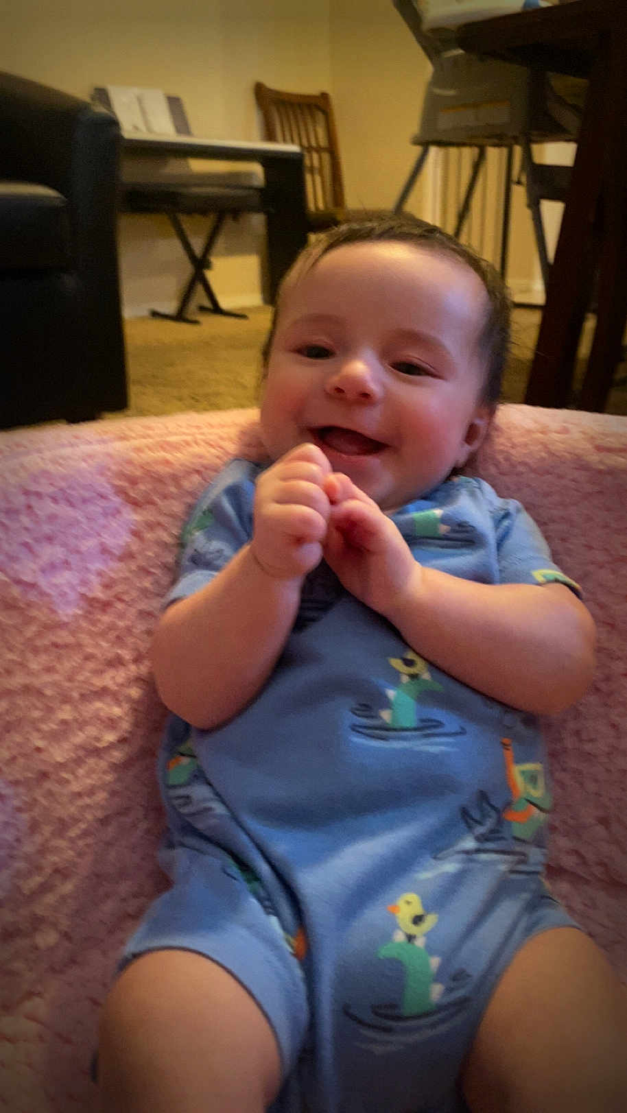 Elijah is registered to the contest to win money with this photo: baby, infant, smile, clapping, blue_onesie, duck_pattern, dinosaur_pattern, pink_blanket, indoor, living_room, carpet, chair, piano, furniture, happy, cute, child, person, portrait, home