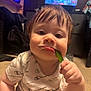 Zayden is registered to the contest to win money with this photo: toddler, child, indoor, person, face, chewing, green_bean, clothing, short_sleeve, carpet, hair, expression, candid, furniture, television, room, hand, sitting, casual, portrait