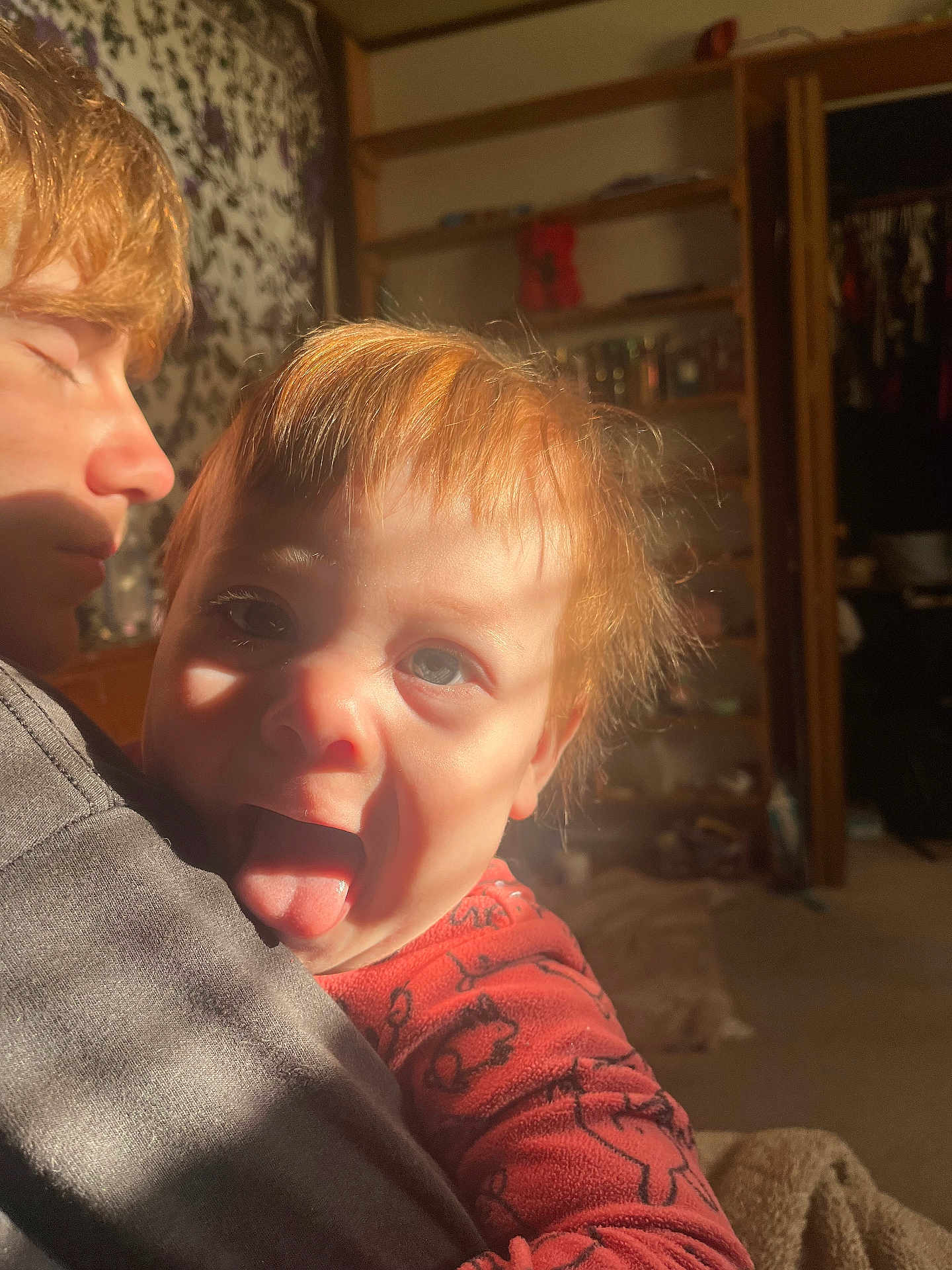 Zayden joined the competition — help win amazing prizes! toddler, child, person, face, tongue, hair, light, shadow, indoor, room, shelf, clothing, holding, young_person, expression, cozy, warm_light, portrait, casual, playful