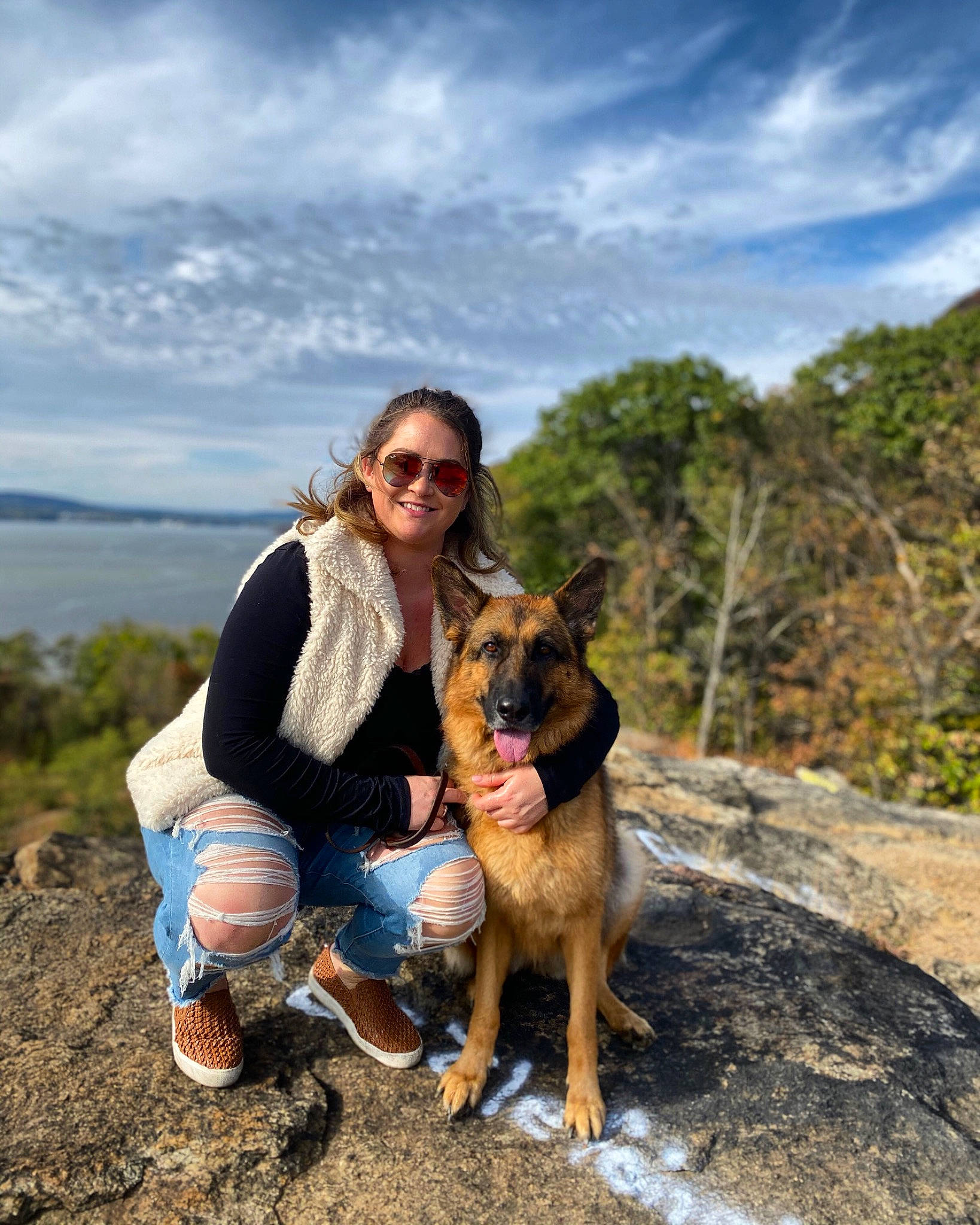 Brandy is registered to the contest to win money with this photo: carnivore, cloud, companion_dog, dog, dog_breed, fawn, goggles, happy, jeans, landscape, mountain, mountainous_landforms, people_in_nature, plant, sky, smile, sunglasses, travel, tree, water