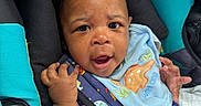Auren is registered to the contest to win money with this photo: baby, black_padding, blanket, blue_bib, car_seat, child, clothing, cute, dinosaur, expression, eyes, face, hand, indoor, infant, person, portrait, seatbelt, teal_padding, young
