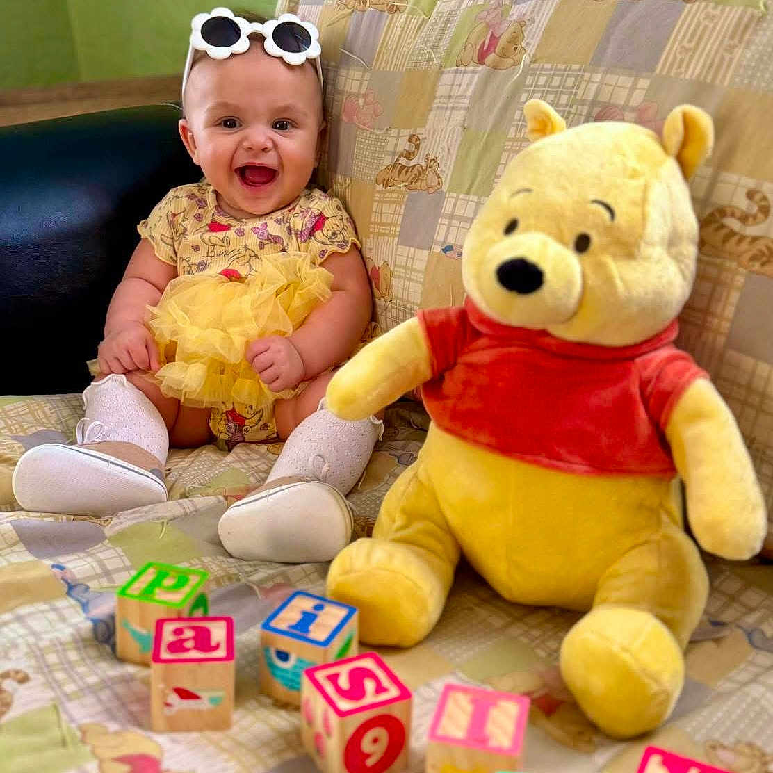 Paisley Mae H. is registered to the contest to win money with this photo: accessories, baby, couch, cushion, face, furniture, happy, head, homedecor, laughing, person, photography, plush, portrait, quilt, sitting, sunglasses, teddybear, text, toy