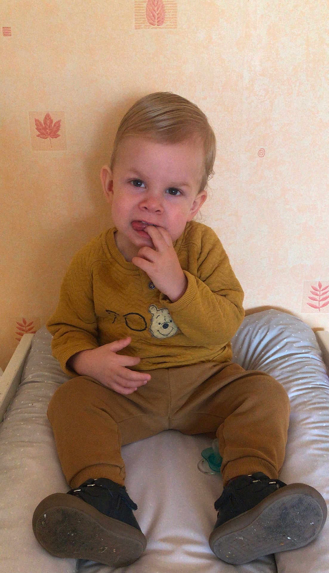 Noah participe au concours pour gagner de l'argent avec cette photo : toddler, child, sitting, indoor, curious, yellow_sweater, brown_pants, black_shoes, finger_in_mouth, wallpaper, leaf_pattern, padded_surface, cute, portrait, person, young_child, expression, clothing, hair, face