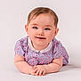 baby, child, infant, smiling, blue_eyes, floral_dress, white_background, portrait, cute, happy, hands, lying_down, soft_lighting, studio_photo, skin, face, head, person, young_child, innocence