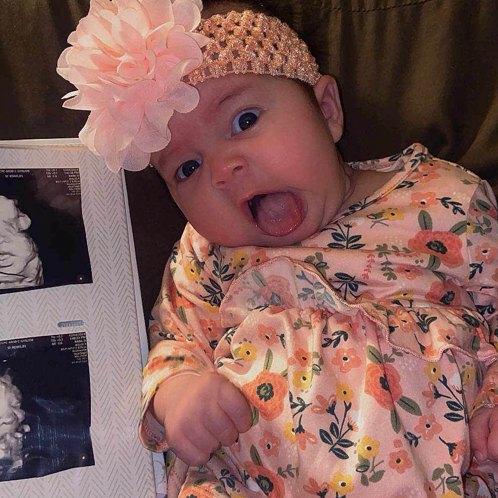 Skyla is registered to the contest to win money with this photo: baby, cap, clothing, couch, cushion, dress, face, flower, furniture, happy, hat, head, homedecor, person, petal, photography, plant, portrait, pottedplant, sitting