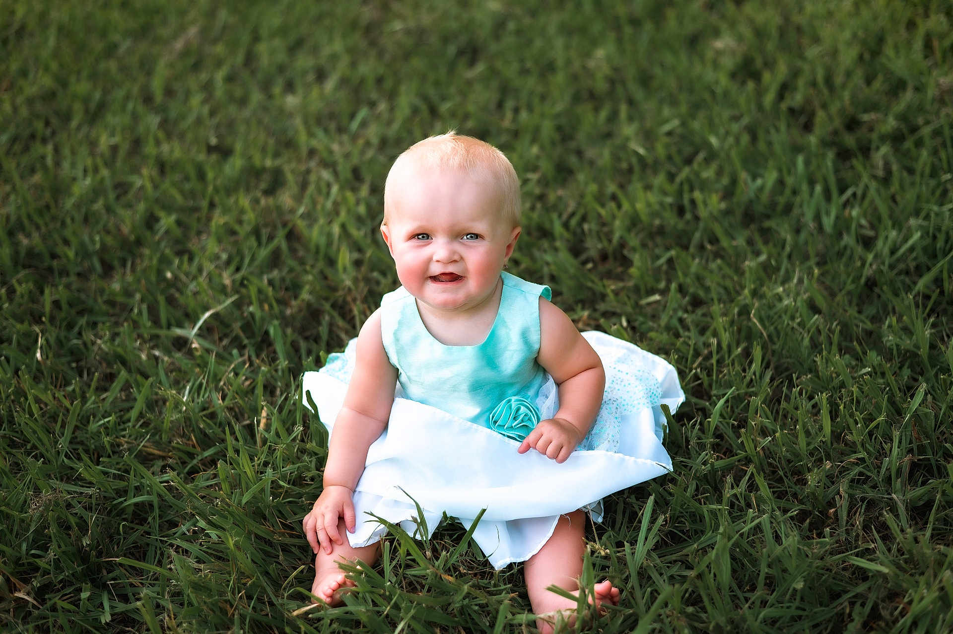 Isla joined the competition — help win amazing prizes! baby, child, grass, outdoor, dress, blue_dress, smile, happy, sitting, barefoot, cute, infant, person, nature, sunlight, greenery, portrait, young_child, summer, playful