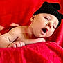 Arthur is registered to the contest to win money with this photo: baby, infant, hat, knitted_hat, black_hat, red_blanket, blanket, lying_down, face, expression, cute, child, skin, headwear, indoors, portrait, closeup, young, small_hands, soft_texture