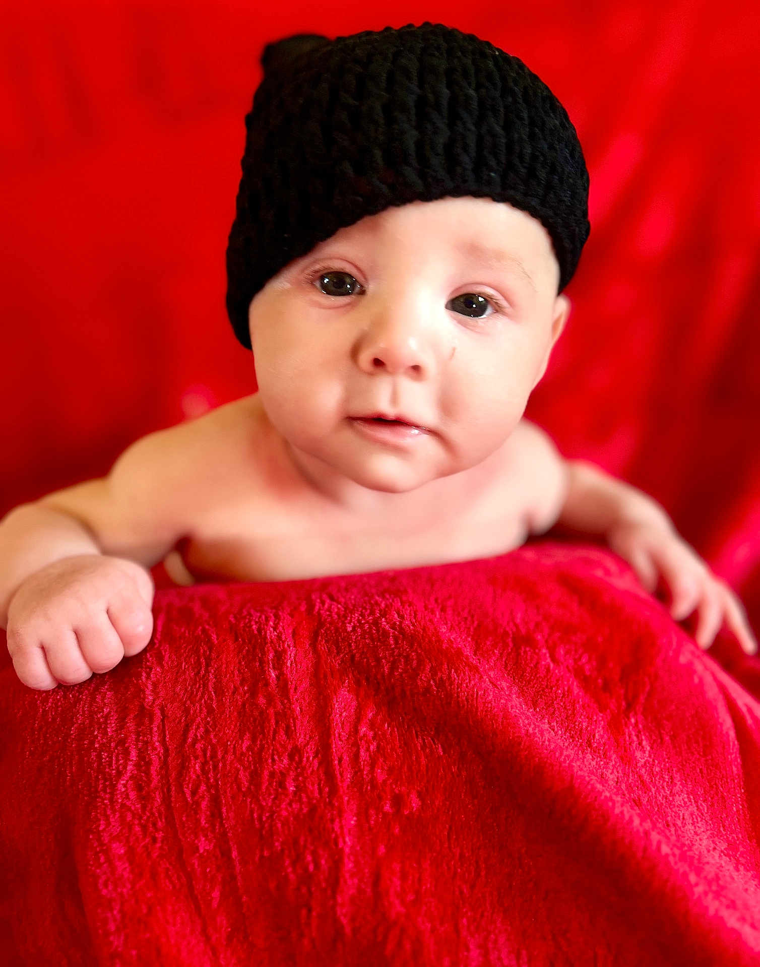 Arthur joined the competition — help win amazing prizes! baby, infant, face, hat, black_hat, red_blanket, red_background, skin, eyes, hand, cute, portrait, child, young, looking, expression, indoors, soft_texture, warm_colors, cozy