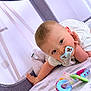 Ismaël participe au concours pour gagner de l'argent avec cette photo : baby, pacifier, toy, playpen, blanket, infant, child, cute, blue, striped_clothing, face, hand, lying_down, indoor, soft_lighting, curious, early_childhood, patterned_blanket, colorful_toy, cozy