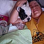 arm, bed, black_spot, blanket, closeup, comfort, cuddle, dog, face, friendship, indoor, nap, person, pet, relaxed, resting, smile, snuggling, white_dog, yellow_shirt