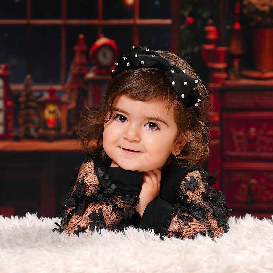 Beyna a rejoint le concours — aidez-le/la à gagner de superbes lots ! background, black_dress, bow, child, curly_hair, cute, decorations, face, fashion, fluffy_surface, girl, happy, holiday_theme, indoor, portrait, posing, smile, toddler, warm_lighting, young_child
