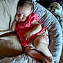 baby, sleeping, infant, pink_clothing, floral_shorts, cushion, pillow, star_pattern, relaxing, indoors, soft_lighting, child, peaceful, resting, cute, person, foot, hand, blanket, fabric