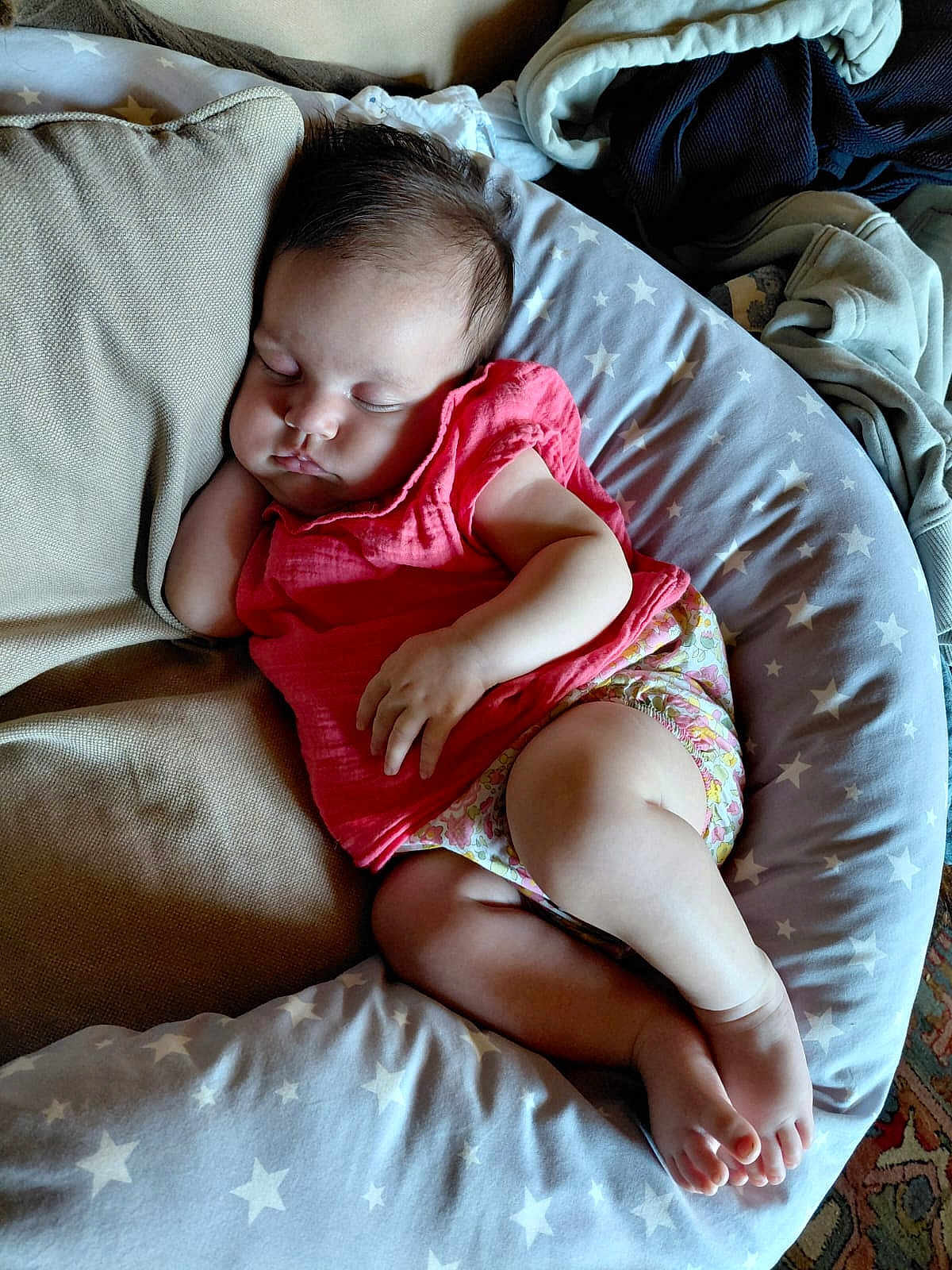 Jeanne a rejoint le concours — aidez-le/la à gagner de superbes lots ! baby, sleeping, infant, pink_clothing, floral_shorts, cushion, pillow, star_pattern, relaxing, indoors, soft_lighting, child, peaceful, resting, cute, person, foot, hand, blanket, fabric