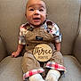 baby, infant, child, plaid_shirt, overalls, socks, wooden_sign, armchair, smiling, happy, seated, indoors, cute, person, face, clothing, fabric, furniture, portrait, three_months