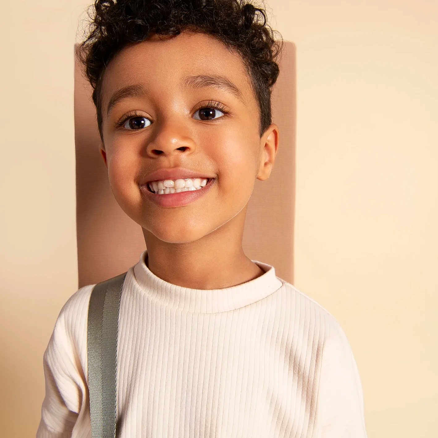 Kelly joined the competition — help win amazing prizes! background, beige, boy, casual, child, clothing, curly_hair, cute, expression, face, fashion, happy, human, indoors, person, portrait, shirt, smiling, strap, young