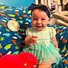 Charlotte is registered to the contest to win money with this photo: baby, child, smiling, blue_headband, mint_green_dress, plush_toy, red_dinosaur, blanket, dinosaur_pattern, happy, indoors, sitting, cute, portrait, infant, toddler, clothing, toy, playful, colorful
