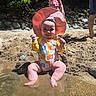 Charlotte is registered to the contest to win money with this photo: baby, child, water, sand, beach, sunhat, swimsuit, sitting, smiling, happy, outdoor, nature, rocks, trees, summer, people, legs, sunlight, play, fun