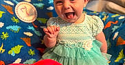 Charlotte joined the competition — help win amazing prizes! baby, child, smiling, happy, headband, dress, toy, plush, red, blue, blanket, dinosaur, pattern, sitting, indoor, cute, infant, playful, tongue_out, person