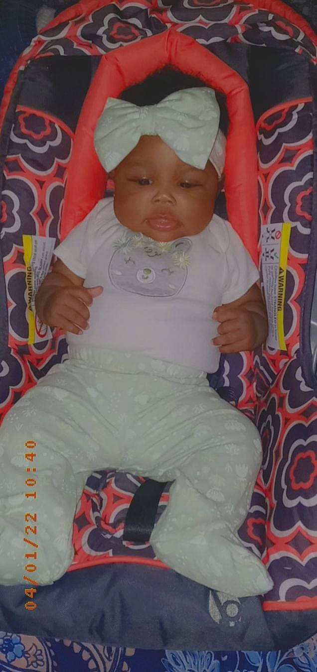 M'Lonie is registered to the contest to win money with this photo: baby, baby_carriage, baby_products, baby_toddler_clothing, cap, carmine, cheek, child, comfort, hand, headwear, lap, lip, magenta, pattern, person, pink, sitting, skin, sleeve