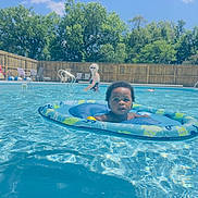 Donald is registered to the contest to win money with this photo: toddler, child, pool, water, inflatable_ring, swimming, summer, outdoor, sunlight, adult, fence, trees, blue_sky, recreation, leisure, vacation, fun, holiday, swimwear, relaxation