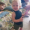 adult, barefoot, black_top, carpet, child, couch, curly_hair, floral_pattern, furniture, happy, home, indoor, person, pillow, pink_croc, playful, seated, shorts, smile, toddler