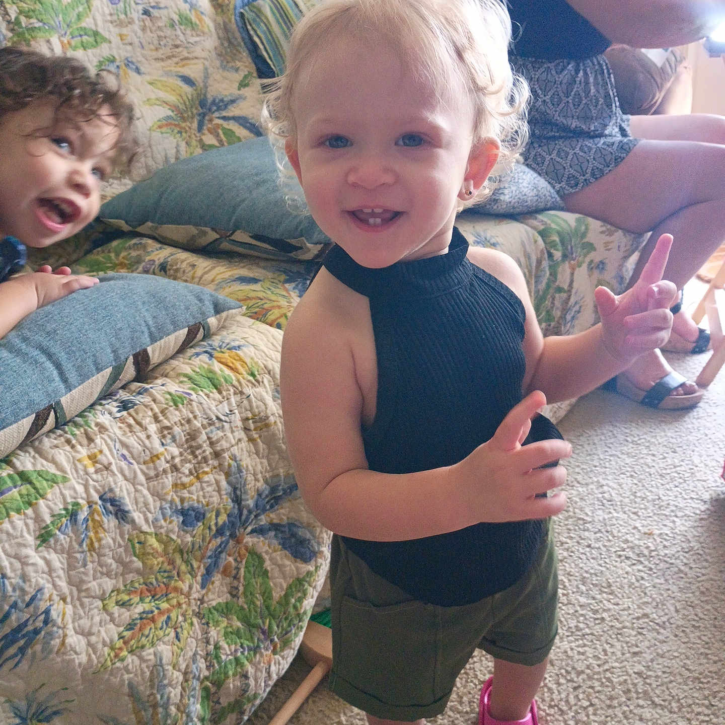 Alyiah joined the competition — help win amazing prizes! adult, barefoot, black_top, carpet, child, couch, curly_hair, floral_pattern, furniture, happy, home, indoor, person, pillow, pink_croc, playful, seated, shorts, smile, toddler
