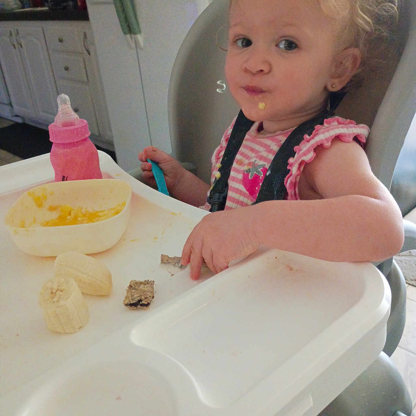 Alyiah is registered to the contest to win money with this photo: toddler, high_chair, food, banana, bottle, kitchen, child, curly_hair, meal_time, baby, face, pink, plastic_bowl, utensil, eating, indoor, person, cute, snack, seat
