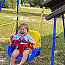 baby, child, swing, playground, outdoor, smiling, laughing, happy, lollipop, infant, sitting, play_equipment, blue, yellow, red, grass, backyard, trees, sunny, portrait