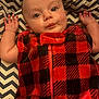Jameson is registered to the contest to win money with this photo: baby, infant, face, eyes, hand, arm, clothing, fleece, red, black, plaid, pattern, blanket, zigzag, person, cute, lying_down, indoor, portrait, child