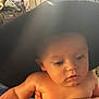 baby, child, face, hat, hand, skin, expression, indoors, person, portrait, curious, closeup, headwear, support, young, infant, human, soft_light, blurry_background, holding