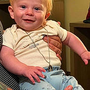 Charlie is registered to the contest to win money with this photo: baby, child, smiling, blue_eyes, red_hair, necklace, pendant, white_shirt, light_blue_pants, animal_prints, tattoo, hand, indoor, person, cute, happy, infant, holding, portrait, clothing