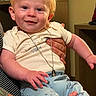 baby, child, smiling, blue_eyes, red_hair, necklace, pendant, white_shirt, light_blue_pants, animal_prints, tattoo, hand, indoor, person, cute, happy, infant, holding, portrait, clothing