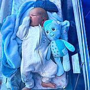 Theo is registered to the contest to win money with this photo: newborn, baby, hospital_bassinet, blanket, plush_toy, onesie, infant, sleeping, cozy, blue, soft, cute, foot, hand, child, bed, resting, indoors, person, baby_clothes