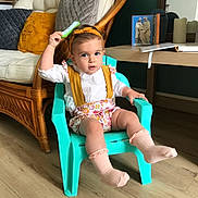 Hortense a rejoint le concours — aidez-le/la à gagner de superbes lots ! child, toddler, chair, comb, headband, socks, floral_outfit, suspenders, turquoise_chair, wicker_chair, cushion, living_room, book, table, wooden_floor, portrait, cute, curious_expression, seat, home_interior