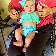 Rosemary joined the competition — help win amazing prizes! baby, child, adult, hands, blue_eyes, headband, swimsuit, sitting, lap, clothing, red_shirt, black_pants, indoor, chair, flooring, person, holding_hands, curious, cute, portrait