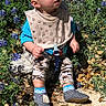 Zander is registered to the contest to win money with this photo: baby, baby_shoes, bib, blue_flowers, camouflage_pants, child, cute, garden, greenery, infant, nature, outdoor, pacifier_clip, portrait, rock, sitting, socks, sunny, toddler, wildflowers