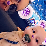 Zander is registered to the contest to win money with this photo: adult, arcade, baby, bib, bokeh, close_up, colorful_lights, face, filter_overlay, glasses, indoor, infant, onesie, pacifier, parent_child, playful, portrait, purple_ears, purple_glitter, selfie